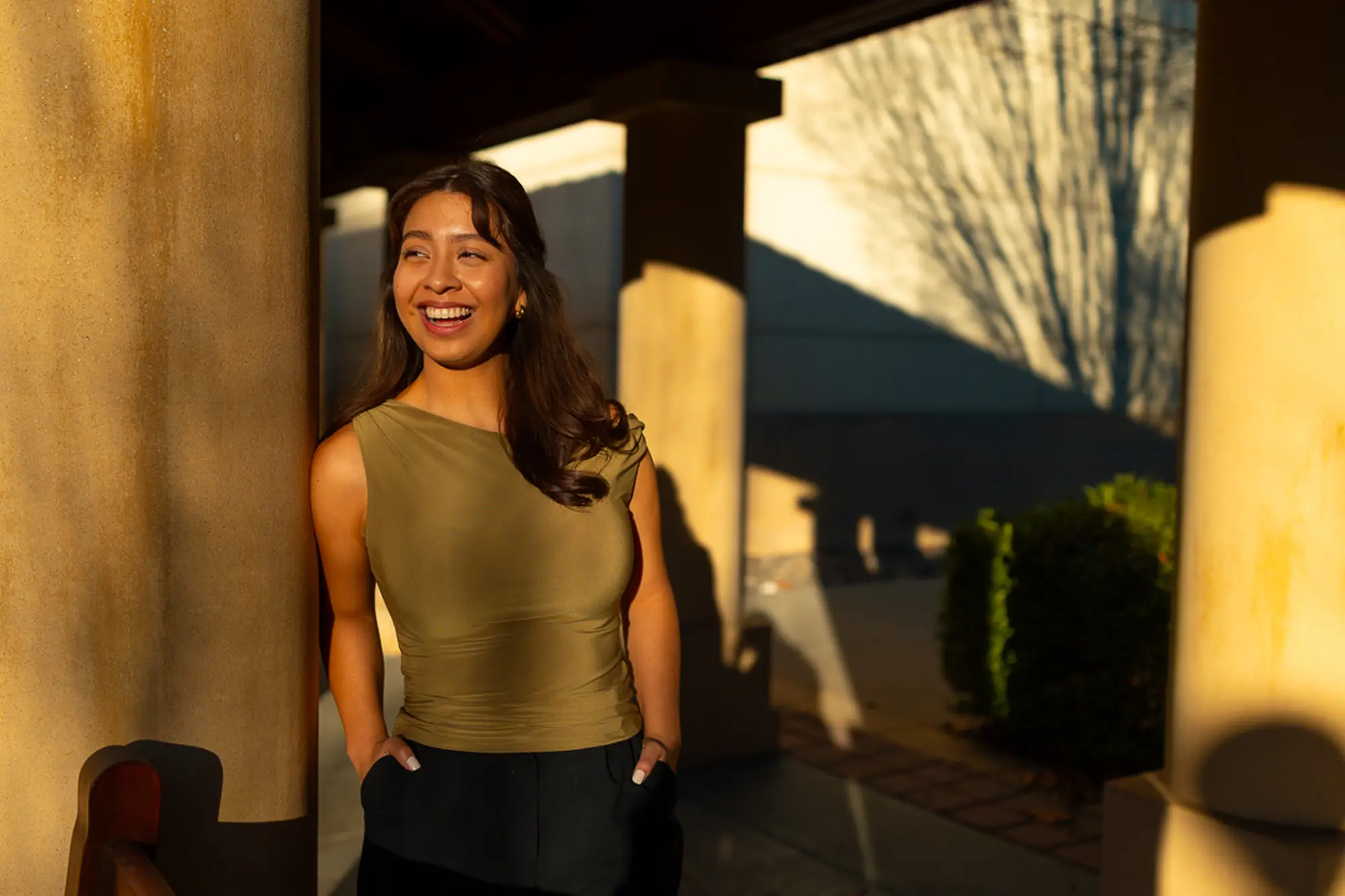An image of Stephanie smiling, leaning up against a concrete pillar.
