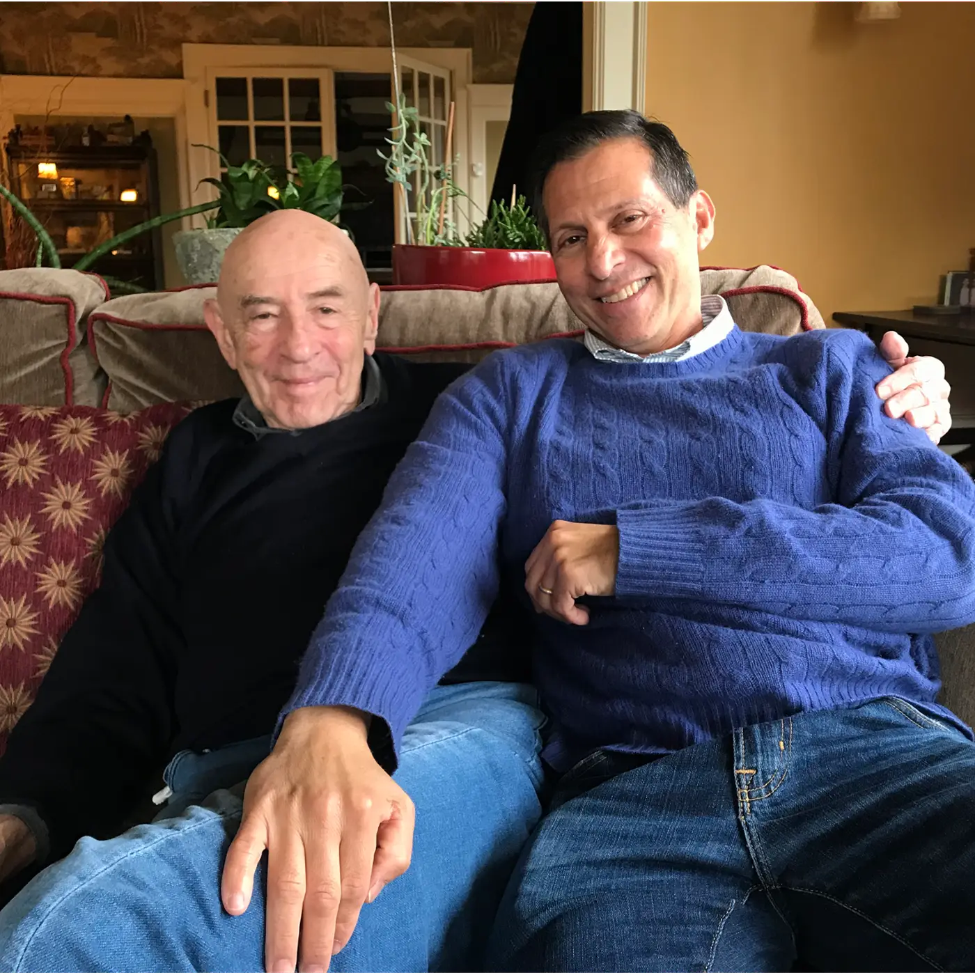 Two men sit together on a couch smiling