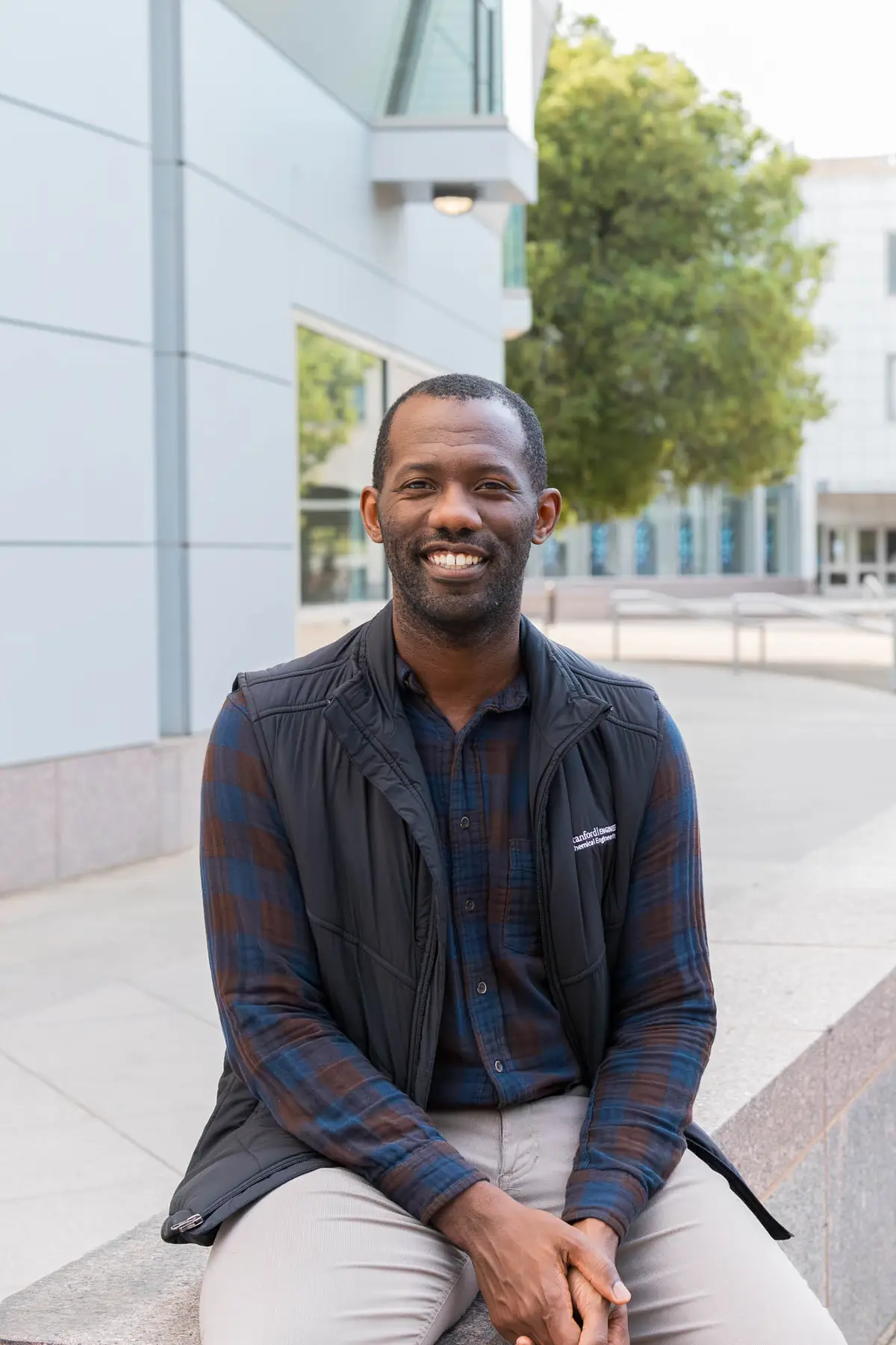 Tarpeh sitting, smiling at the camera with a white building and greenery behind him.