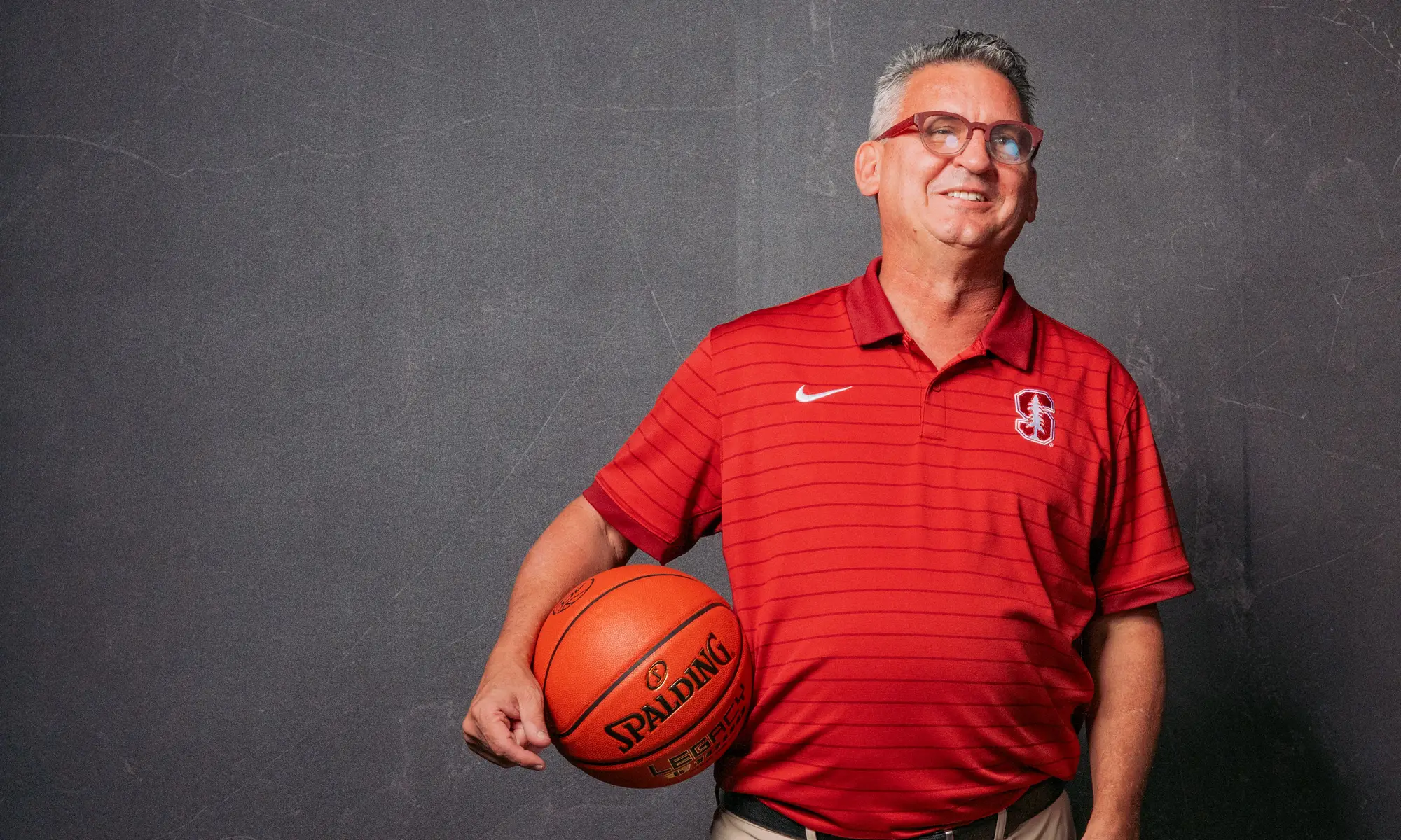 Kyle Smith smiling and posing for the camera with a basketball under his right arm.