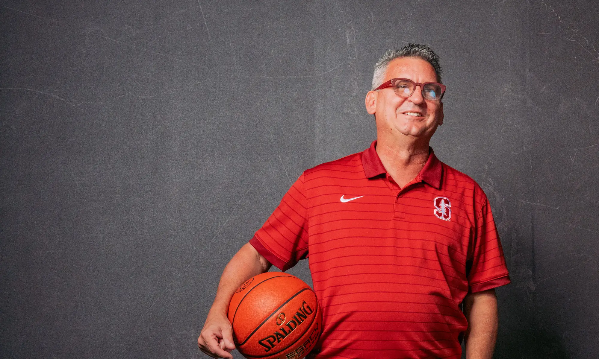 Kyle Smith smiling and posing for the camera with a basketball under his right arm.