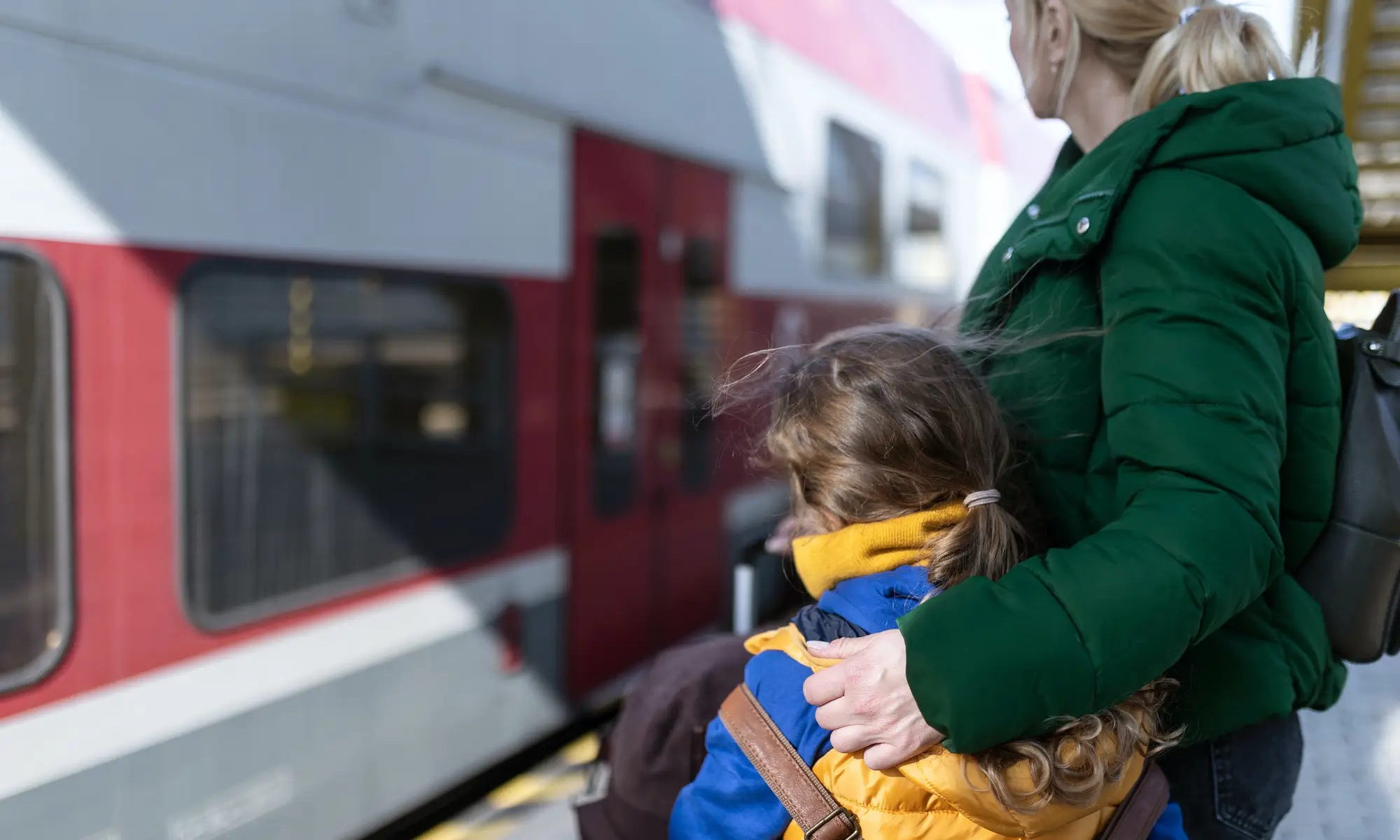 A mom wraps her arm around her daughter as they wait for a train