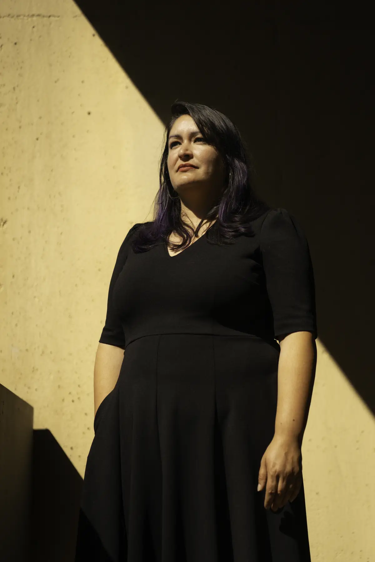 Maria stands in a black dress in front of a shadowy wall