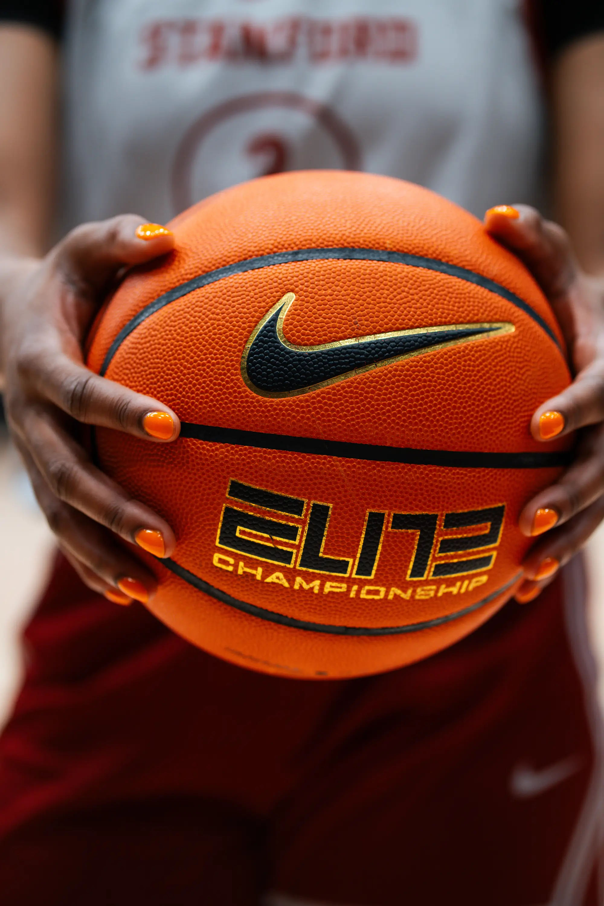 A closeup of Nunu holding a basketball with orange fingernails. 