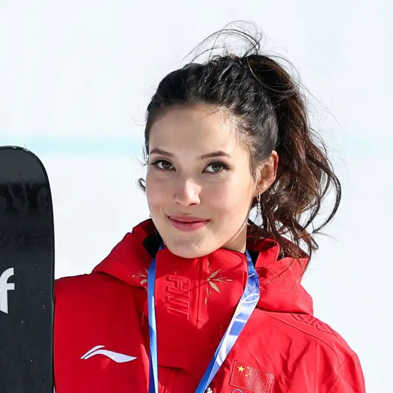 Eileen Gu stands holding her skis and wearing a medal around her neck.