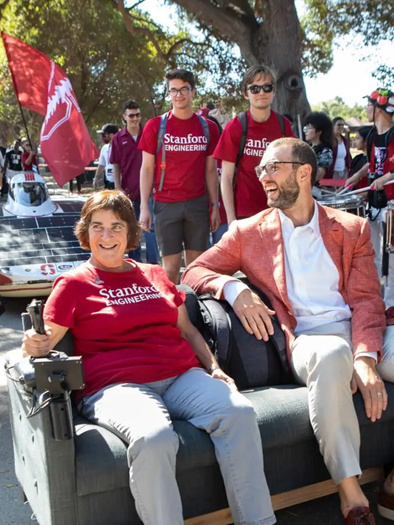 Former provost Persis Drell and Andrew Luck ride a motorized couch through campus.