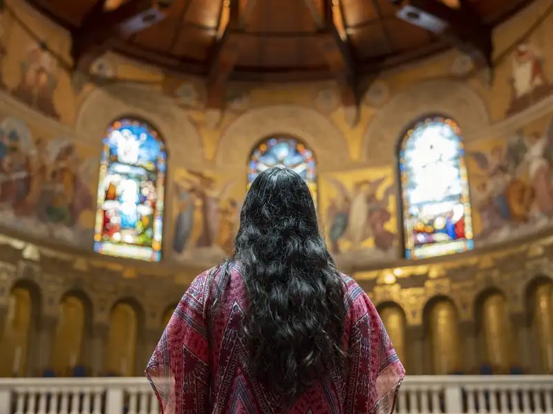 A woman looks at beautiful golden mosaics and stained glass windows inside Memorial Church.