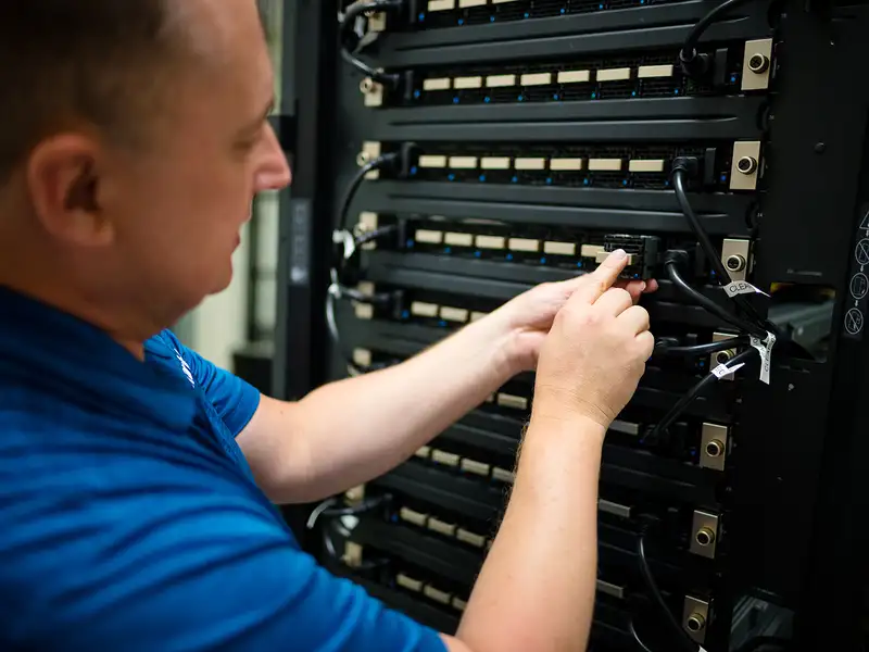 A technician connects cables on a server rack, focusing on organizing data connections in a tech environment.