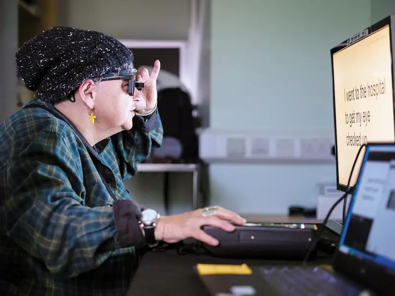 Woman wearing dark glasses uses a large-text computer monitor with assistive technology.