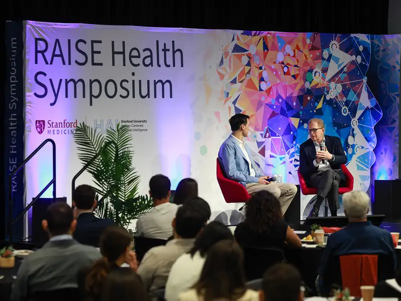 Two speakers discuss topics on stage at the RAISE Health Symposium.