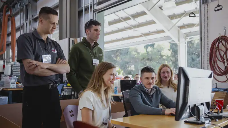 A group of students collaborates and observes while working on a computer in an educational workshop setting.