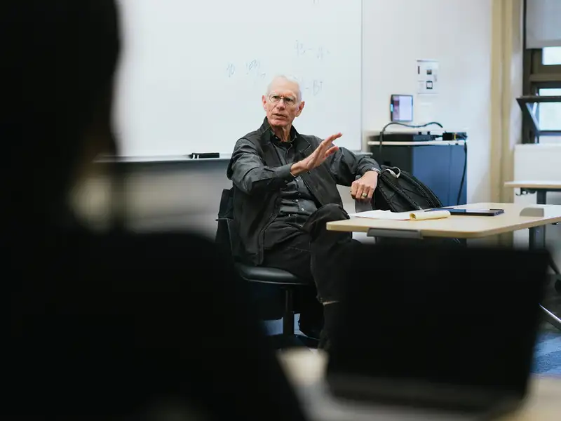 Josiah Ober gestures while speaking to students from his seat at the front of a classroom.