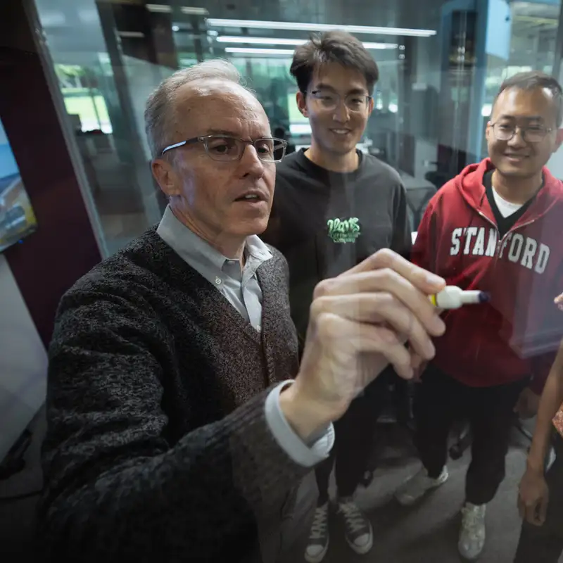 Curtis Langlotz writes on a glass board with a marker while three students look on in an academic setting.