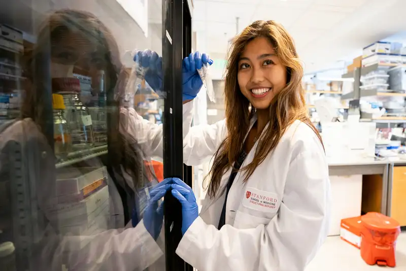 Helena Zhang smiles over her shoulder while retrieving a sample from a lab refrigerator.