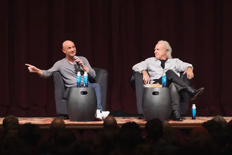 Andre Agassi gestures with a microphone during an onstage conversation with a seated interviewer.