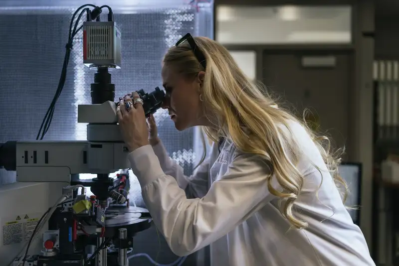 Annie Goettemoeller peers through a microscope in a darkened lab, laser safety glasses pushed up on her head.