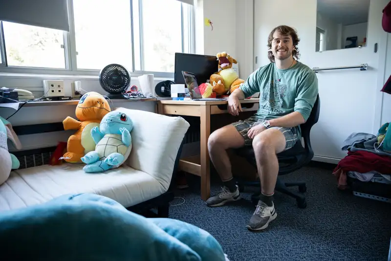 Student at his desk in his dorm room with dinosaur stuffed animals