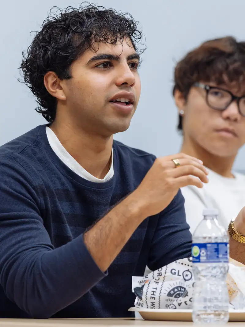 Two individuals engaged in conversation at a table with food and drinks, in a casual meeting setting.