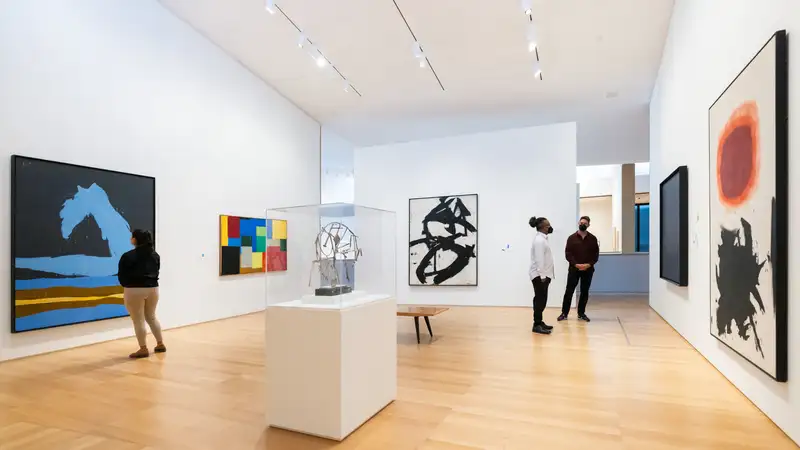 Art exhibit with three people observing the admiring the art displayed on the walls.
