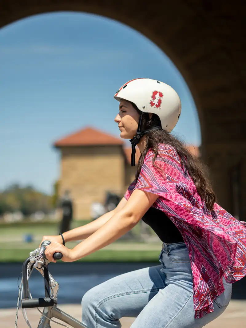 Student riding a bicycle by the quad with a Stanford-branded helmet