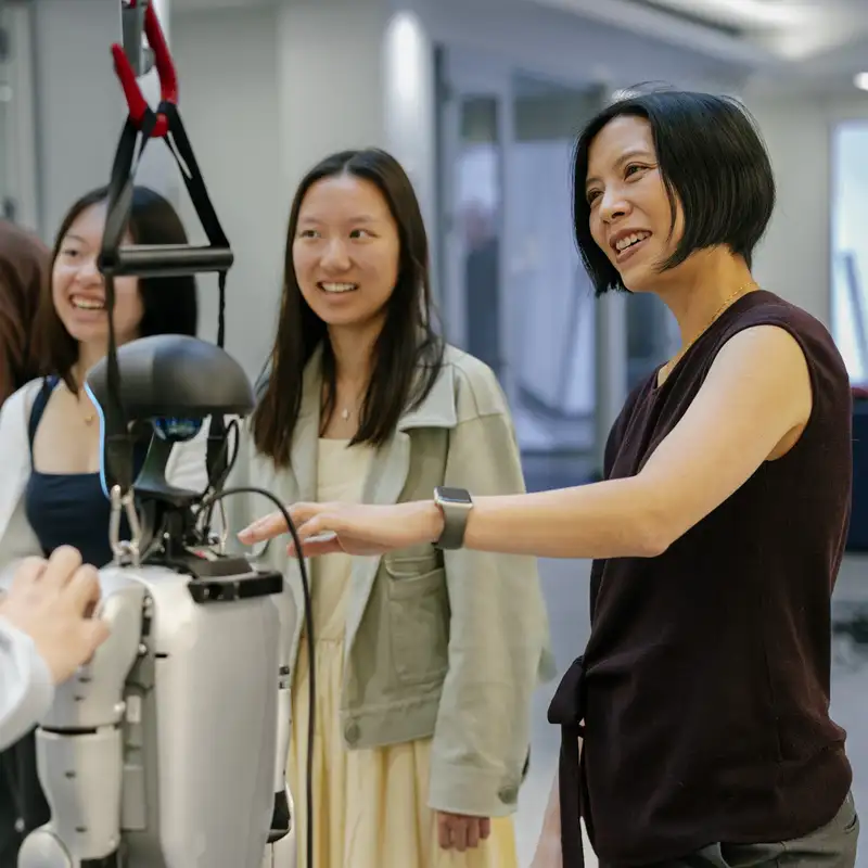 Karen Liu and a group of students gathered around a humanoid robot in a lab setting.
