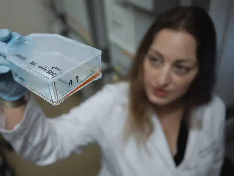 A female researcher hold up a plastic container with a medical sample inside