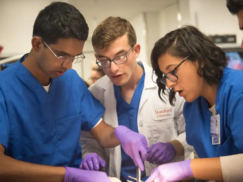 A group of Stanford medical students huddle together over a dissection, focused intently on their work in a clinical anatomy lab.