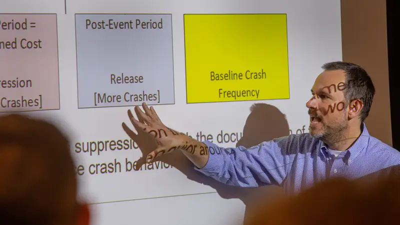 A presenter points to a slide discussing baseline crash frequency during a lecture