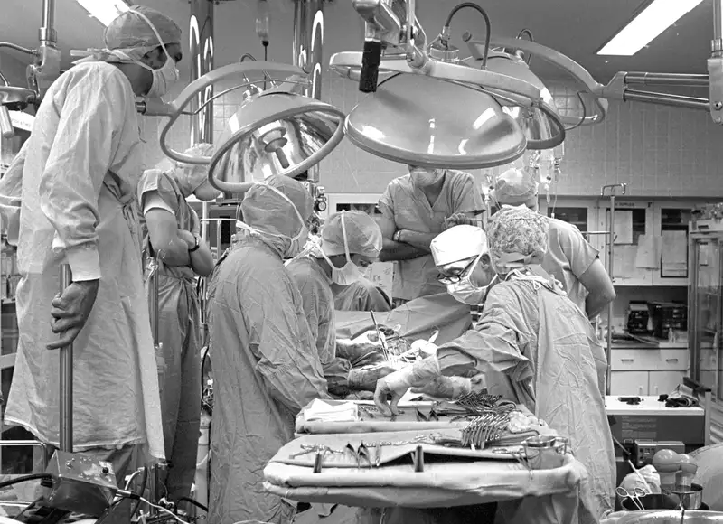 Professor Bruce Reitz and his surgical team in scrubs and masks, focused on a surgery under bright operating room lights and surrounded by medical equipment.