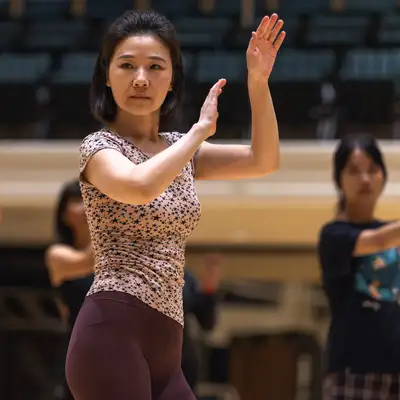 A group of dancers practice in a spacious studio, focusing on their movements with one dancer in the foreground leading the routine.