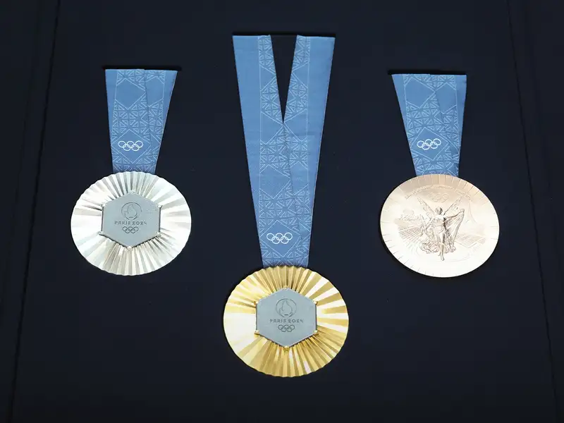 Olympic medals laid out on a black background silver, gold and then bronze.