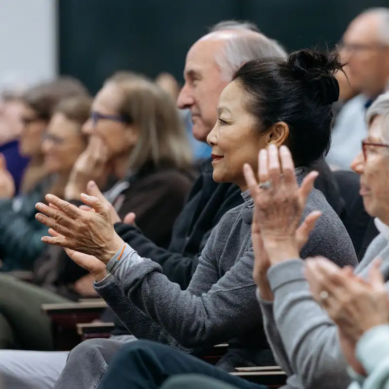 A diverse crowd of people clapping and showing appreciation during an event or presentation.