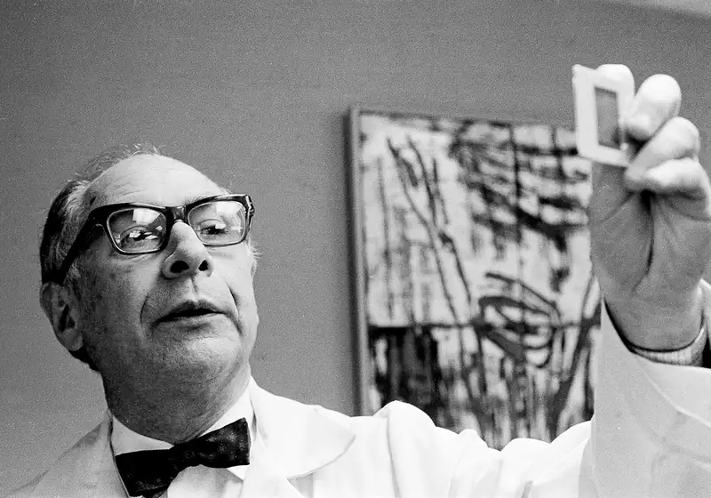 Henry Kaplan holds a small slide while standing in a clinical setting.