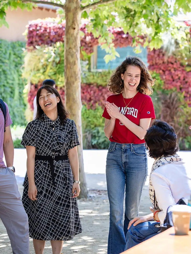 A group of students engaged in conversation outdoors, with a vibrant green and floral backdrop.