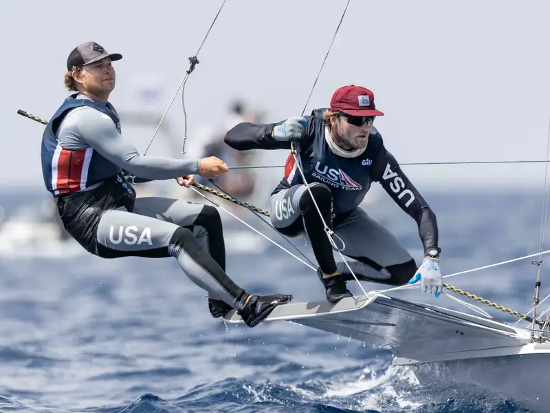 Two members of the U.S. men's sailing team pull on cables as they steer their boat across the water