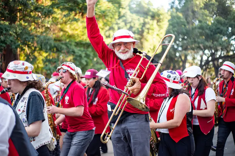 Hal Nystrom, '77, carrying a trombone and waving at the crowd as he marches with students in the Leland Stanford Junior University Marching Band on the way the to the stadium.