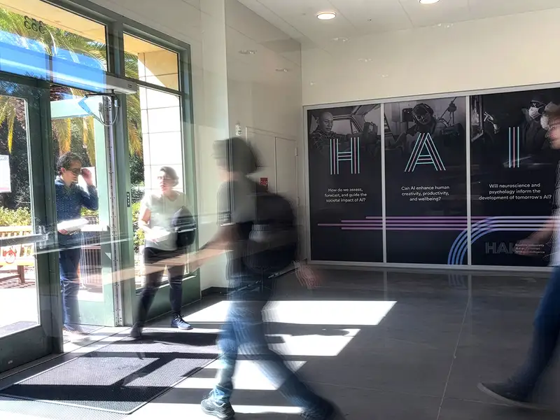 People enter a building displaying wall graphics about AI's societal impact, with a focus on creativity and well-being.