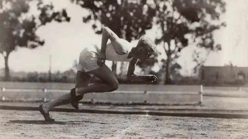 Ben Eastman explodes from a sprint start on a dirt track, body low and driving forward, in this black-and-white historical photo.
