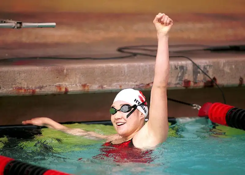 Misty Hyman raises her fist in celebration in the pool after a race, wearing a swim cap with her name and goggles, smiling.