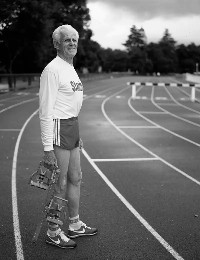 Black and white photo of longtime Stanford track and field coach Payton Jordan, who led the 1968 U.S. Olympic team standing on the track holding a starting block.