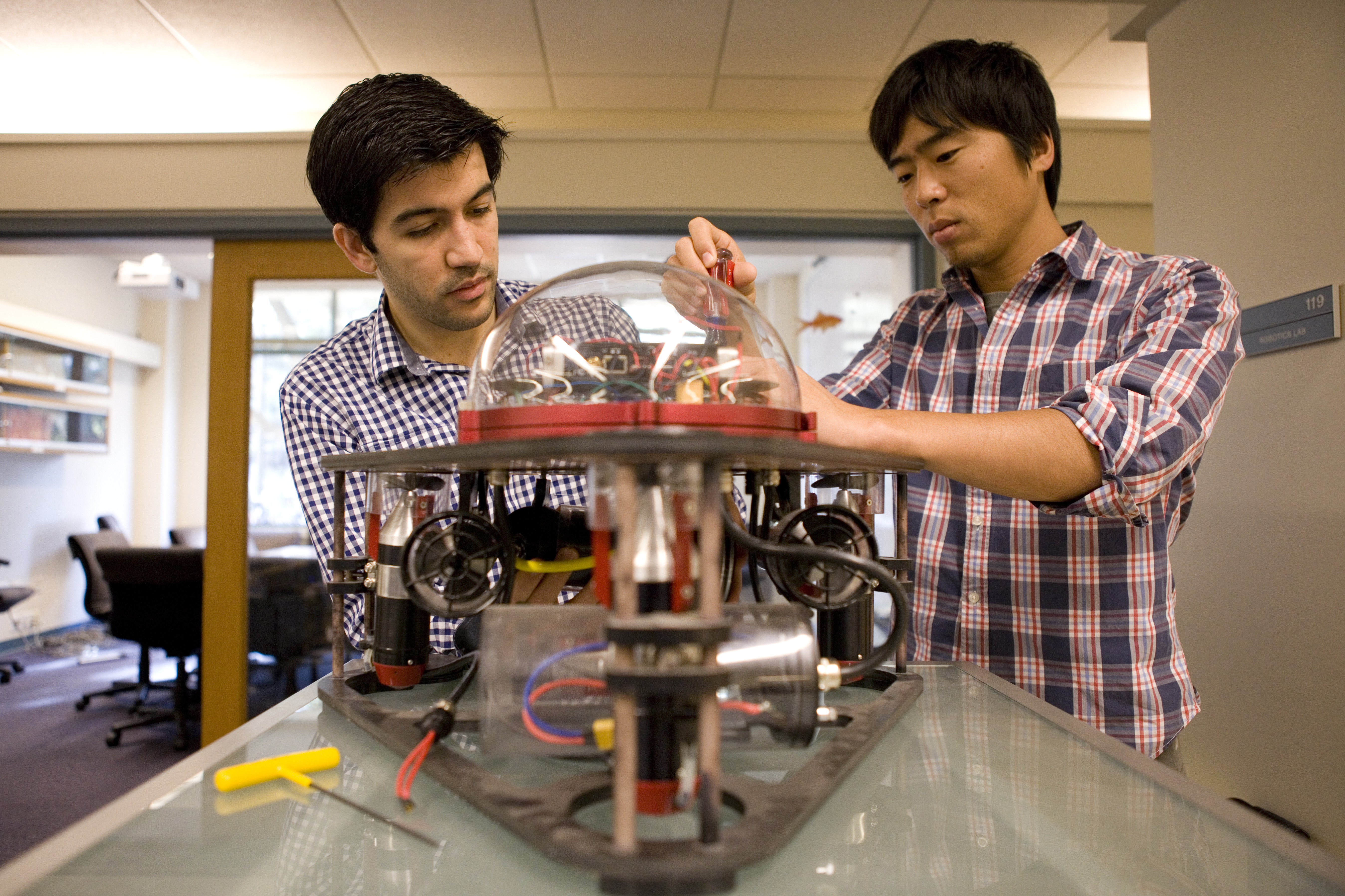Two students work on a mechanical robot with tools