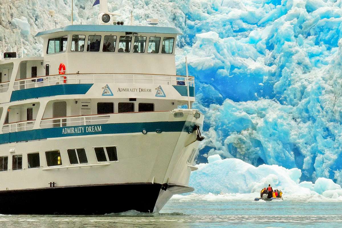 ship at sea in front of massive glacier with small boat
