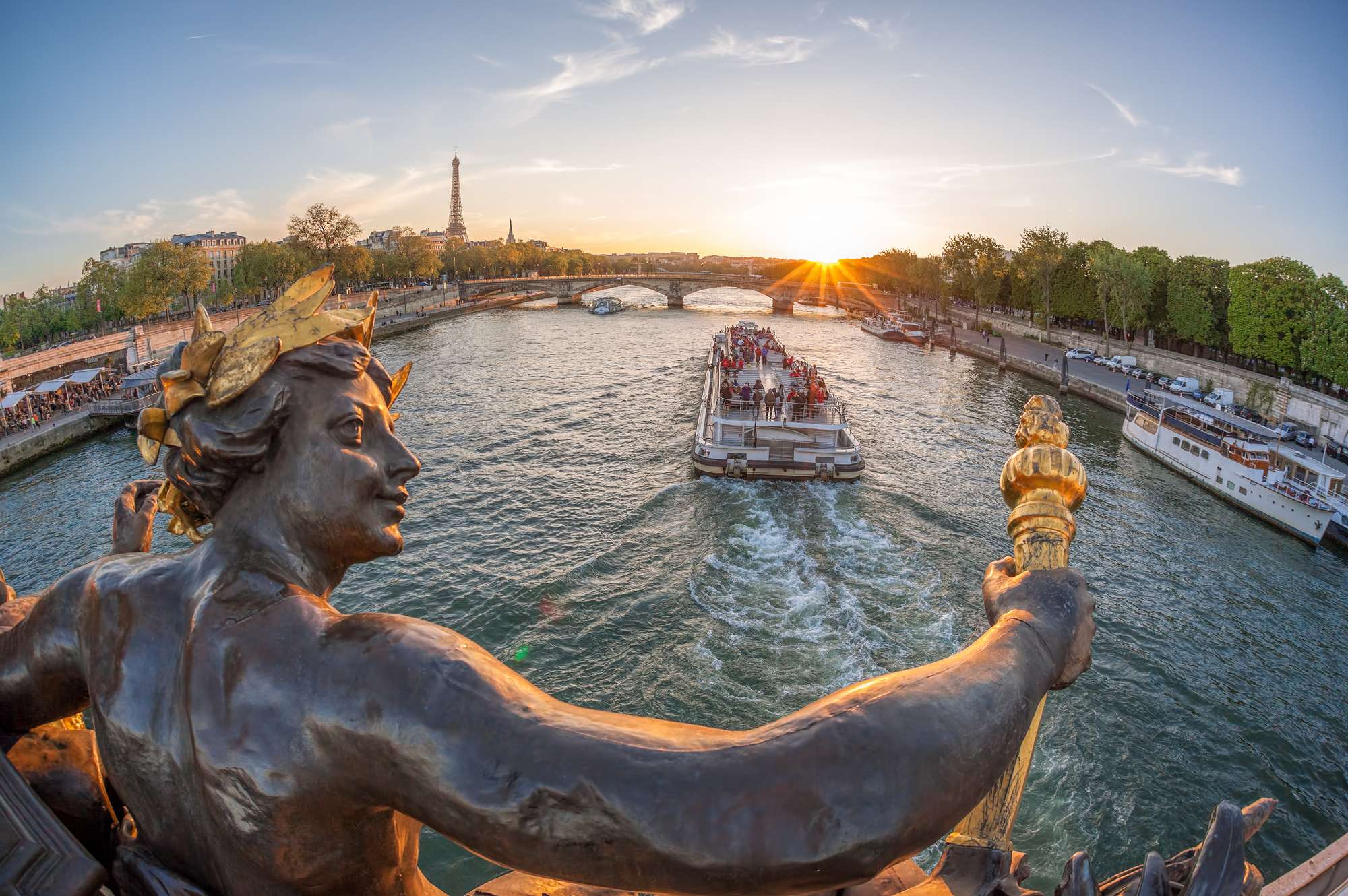 sunset view of statue in foreground with river boat 