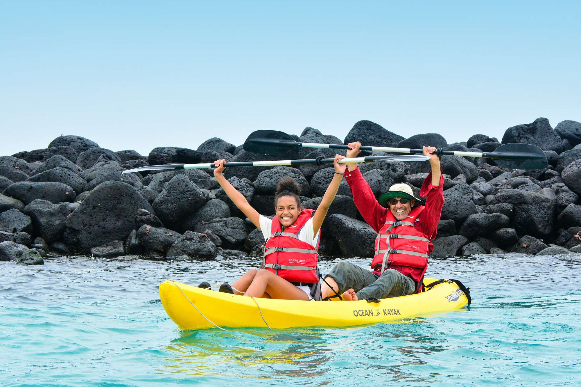 father and daughter in yellow kayak with their paddles raised above head