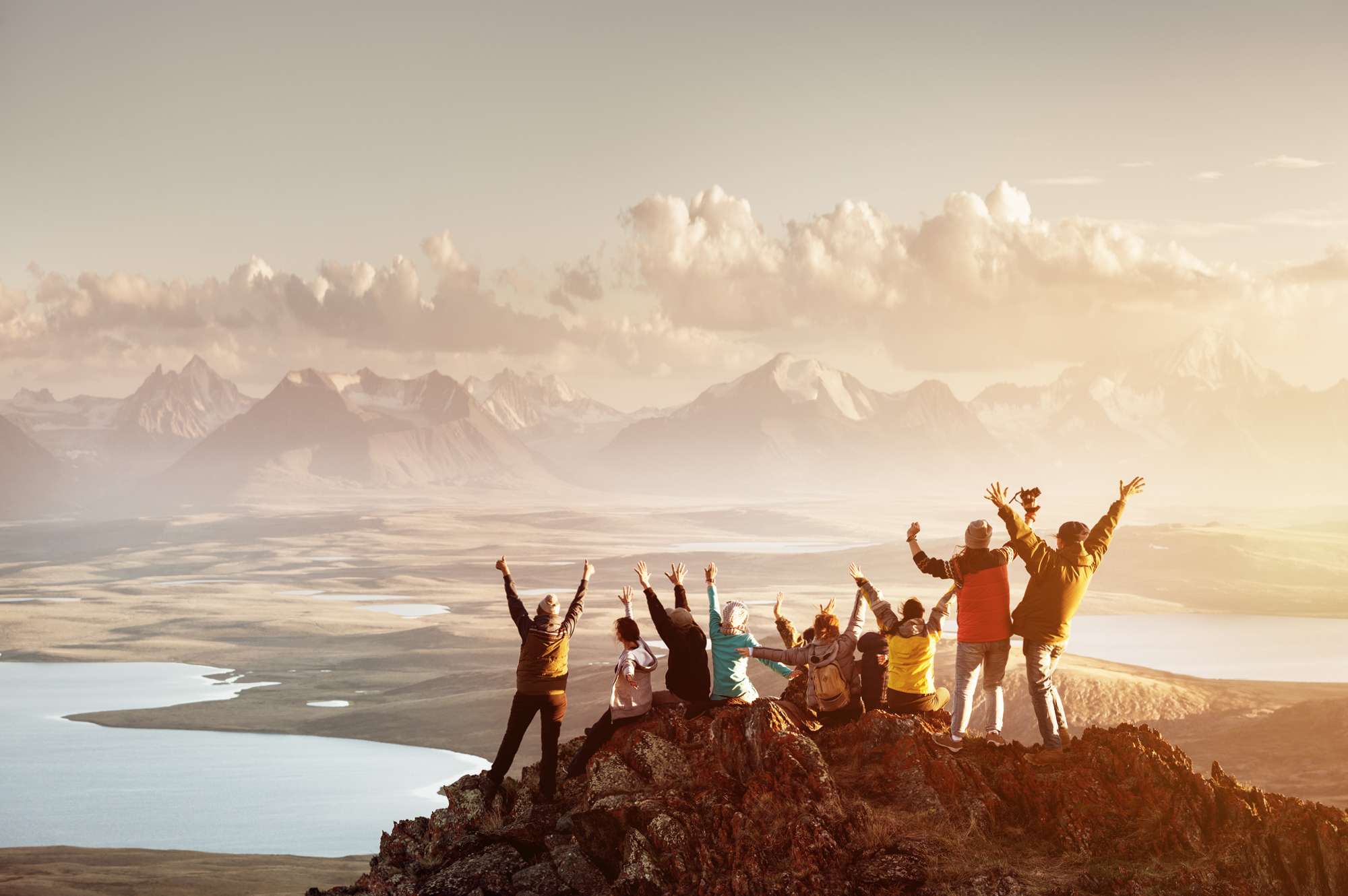 group of people standing on mountain top with hands in the air