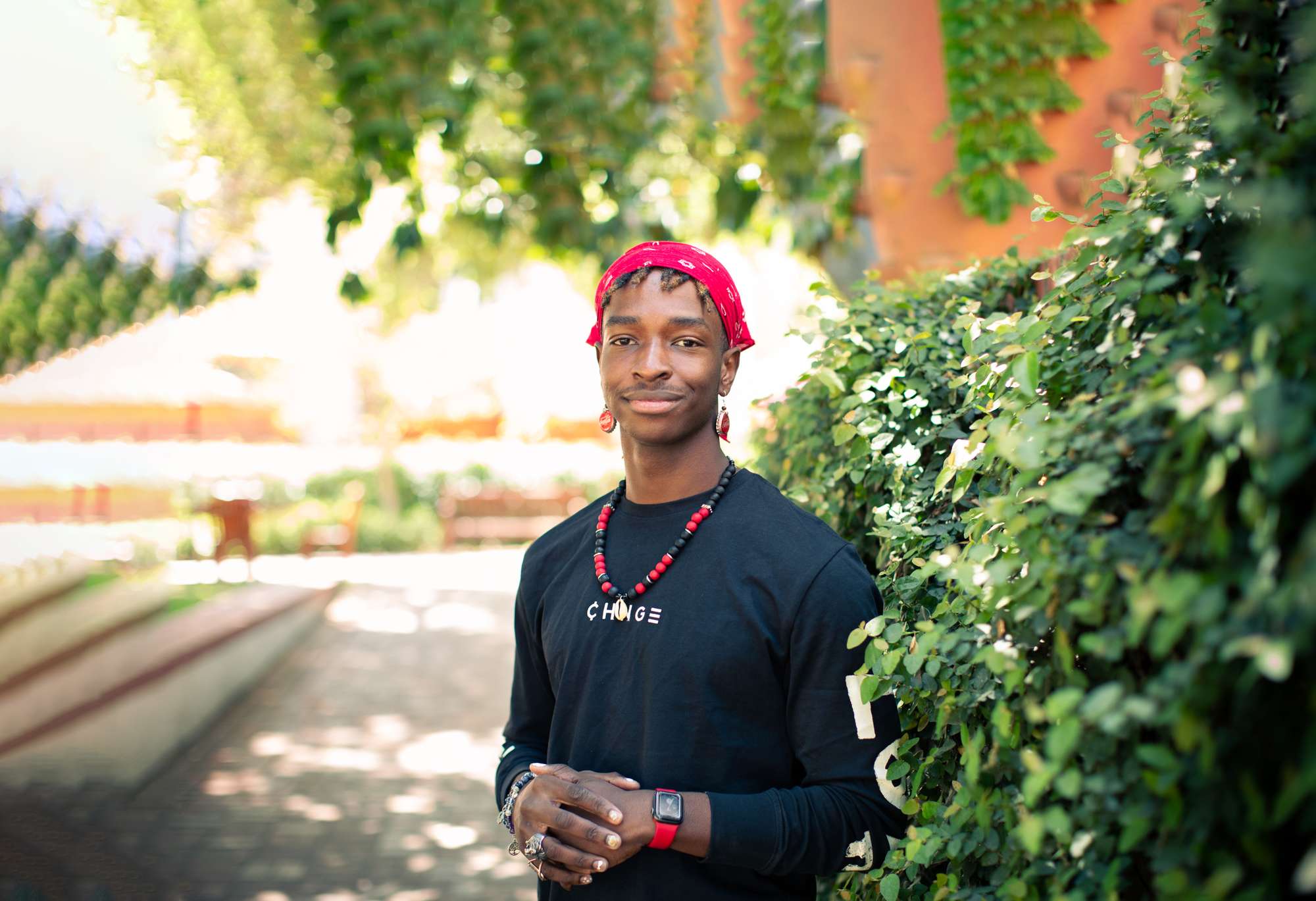 John Okhiulu wearing a red bandana and red-accented jewelry smiles beatific smile on the Stanford campus