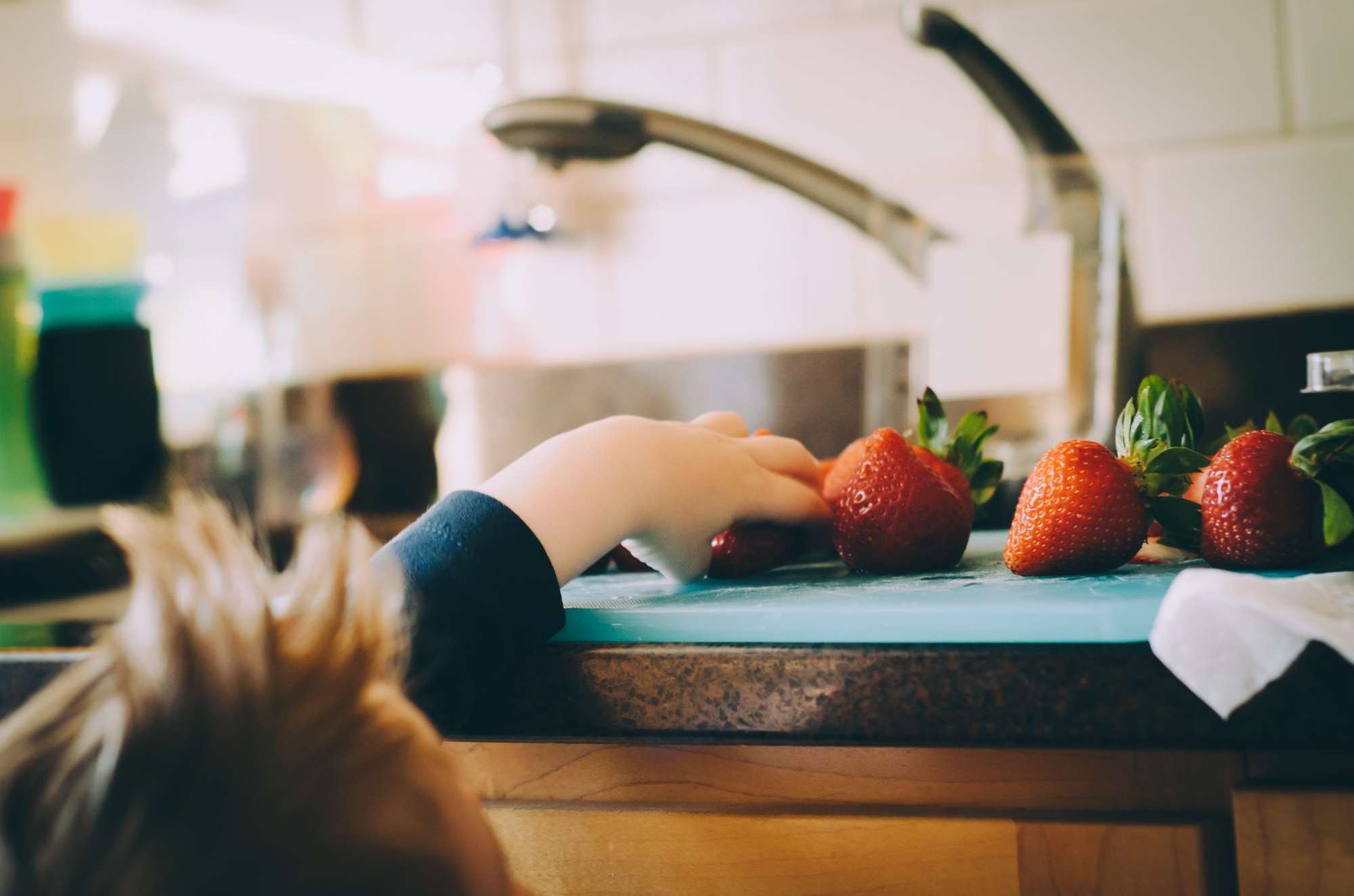 A young boy grabs a strawberry off the kitchen counter