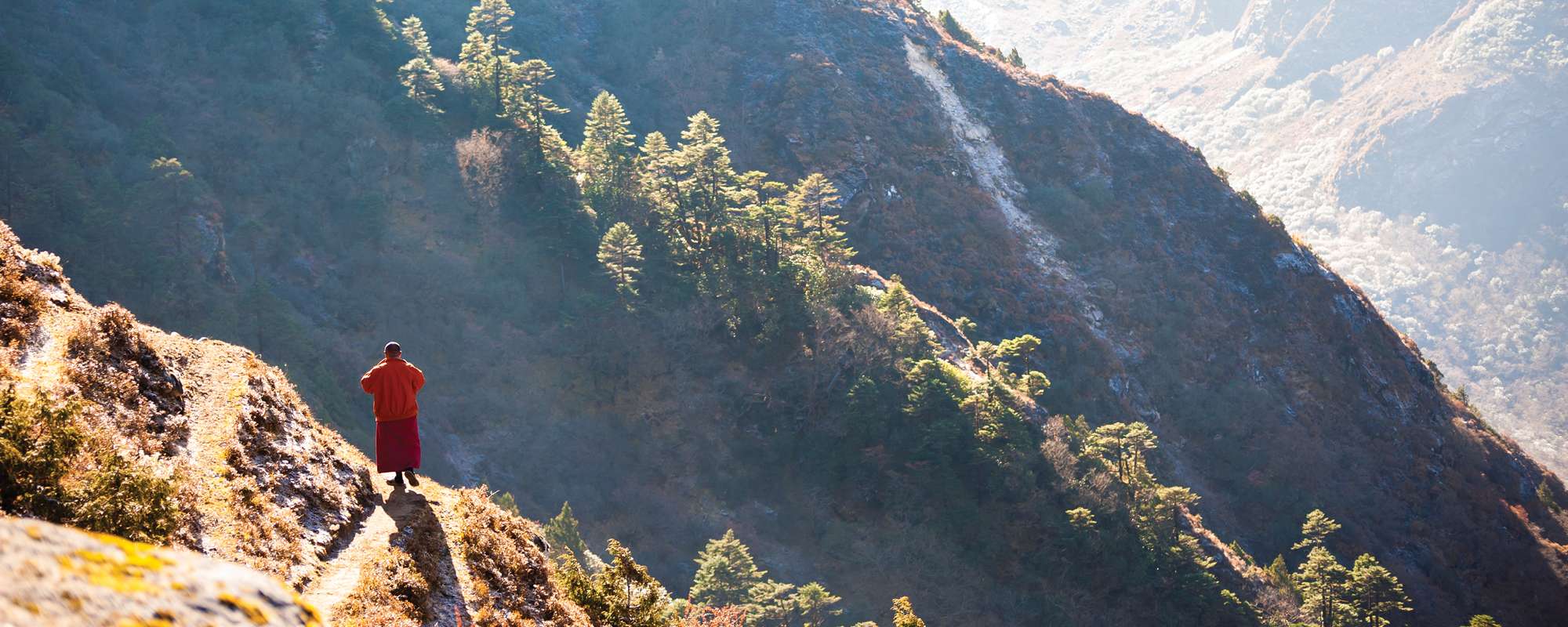 monk standing cliffside viewing valley of mountains