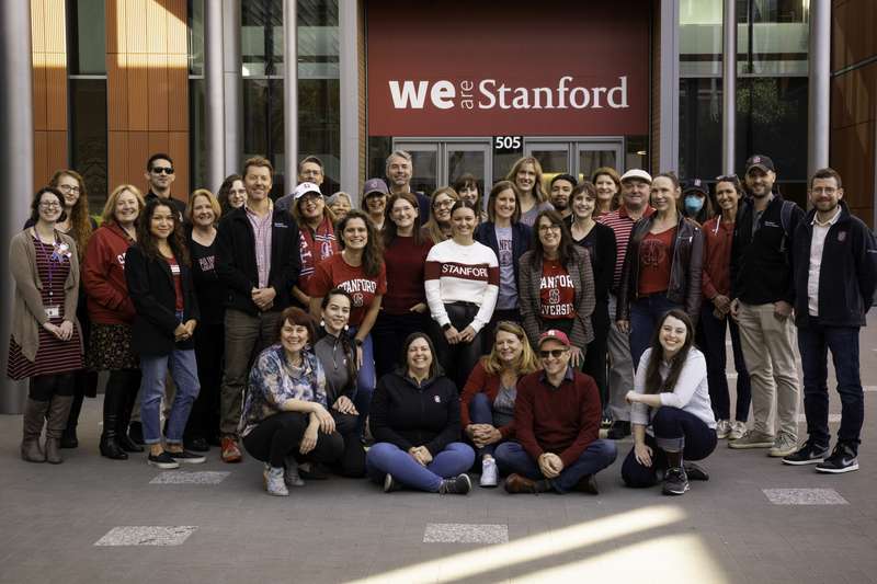A group of OOD staffers smile in front of a sign that says we are stanford